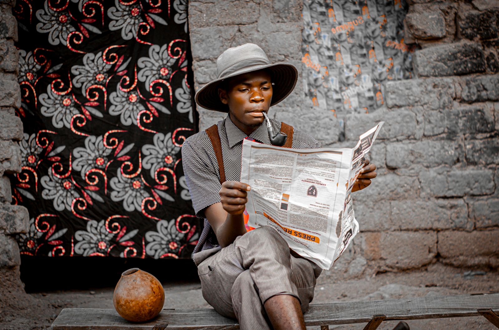 Un homme en tenue traditionnelle lit un journal sur fond de paysages colorés à Blantyre, au Malawi.